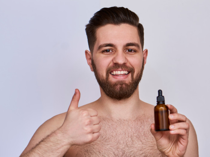 A young smiling man holding a bottle of essential oil