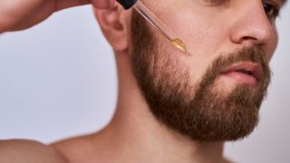 A man with a beard applying oil using a dropper