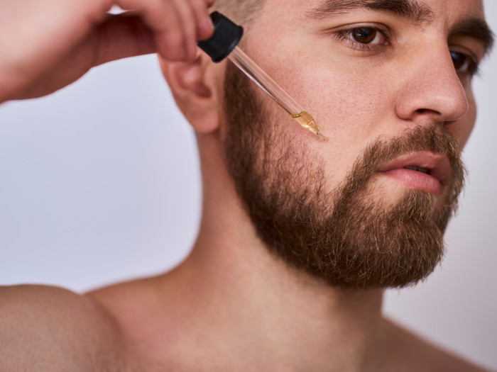 A man with a beard applying oil using a dropper