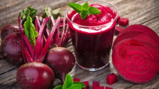 Beetroots, cut beets and a glass of beet juice, placed on a rough wooden surface.