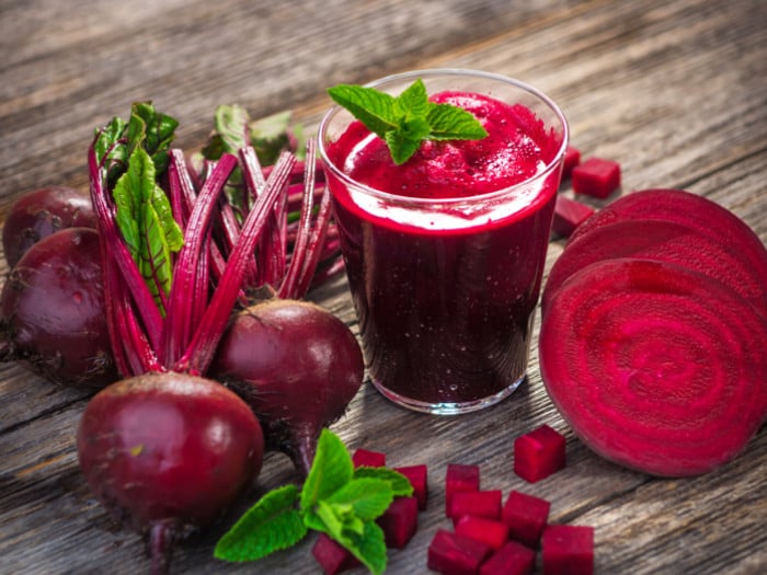 Beetroots, cut beets and a glass of beet juice, placed on a rough wooden surface.