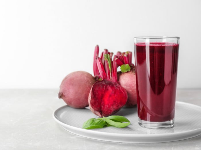 A glass of beet juice with whole beets placed on a white plate