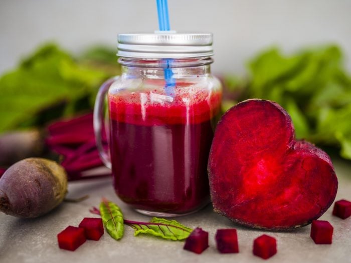 Jar of beetroot juice alongside a heart-shaped piece of beet with beet cubes scattered at the front and blurred beets at the back.