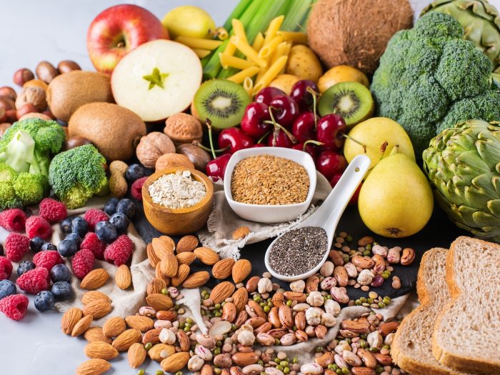 Vegan-friendly foods like nuts, fruits, vegetables, beans, and bread on a white counter