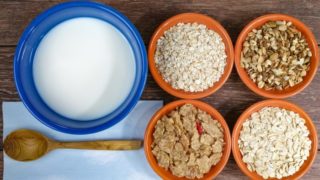 Different varieties of cereal in bowls next to a bowl of milk and a wooden spoon