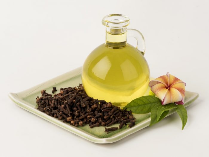 Essential oil bottle with cloves and a flower on a white dish