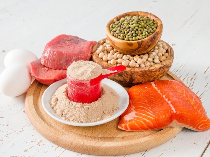 A salmon fillet, protein powder, legumes, meat loaf, and two eggs kept on a round wooden tray