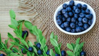 A white bowl of fresh bilberries with leaves on a wooden table