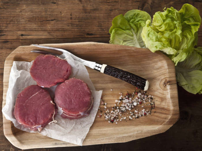 Chunks of bison meat with a roast fork on a wooden tray