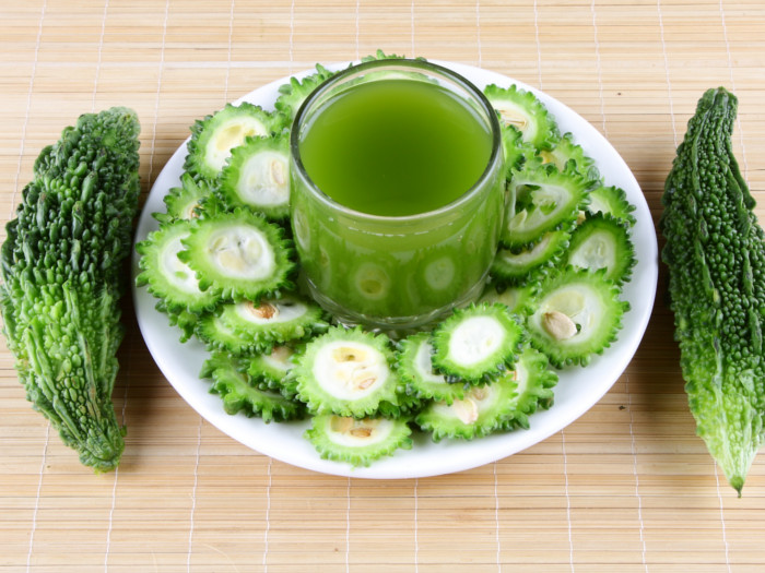 Bitter melons, whole and sliced, and a glass of bitter melon juice on a wooden counter