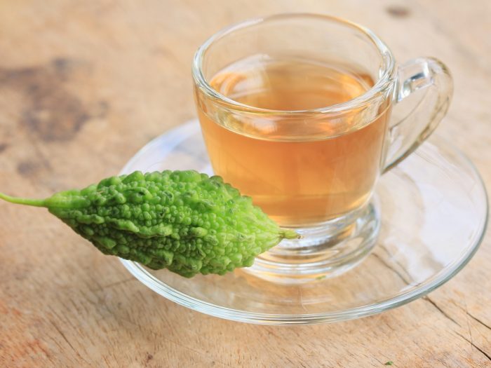 A transparent cup of bitter melon tea with a fresh bitter melon on a wooden table