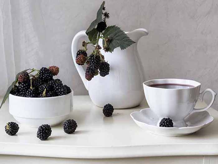 A bowl of blackberries, teapot with blackberries, and a cup and saucer of blackberry tea