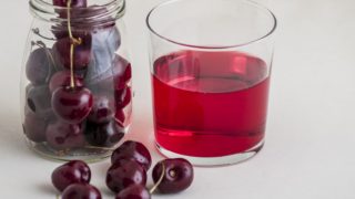 A glass of black cherry juice kept next to a jar of black cherries.