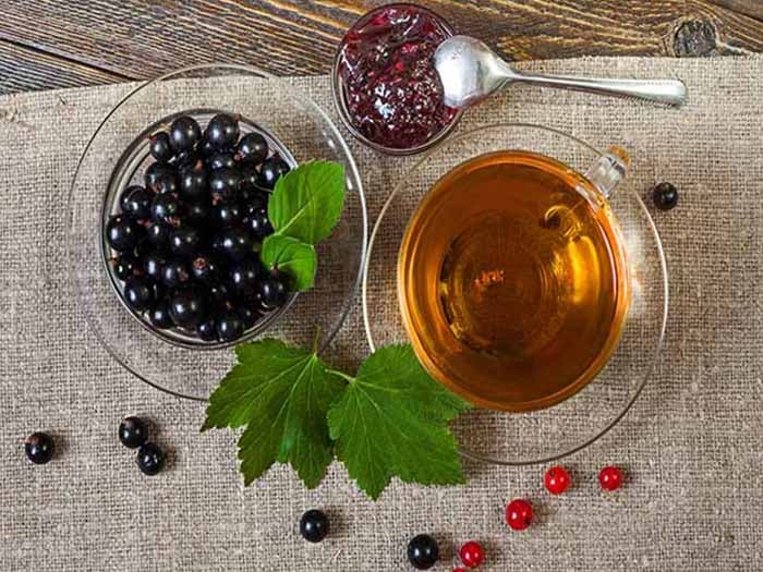 Black currant tea in a cup, next to blackcurrant fruits in a cup, and blackcurrant leaves on a table