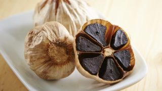 Whole and halved black garlic in a white dish on wood