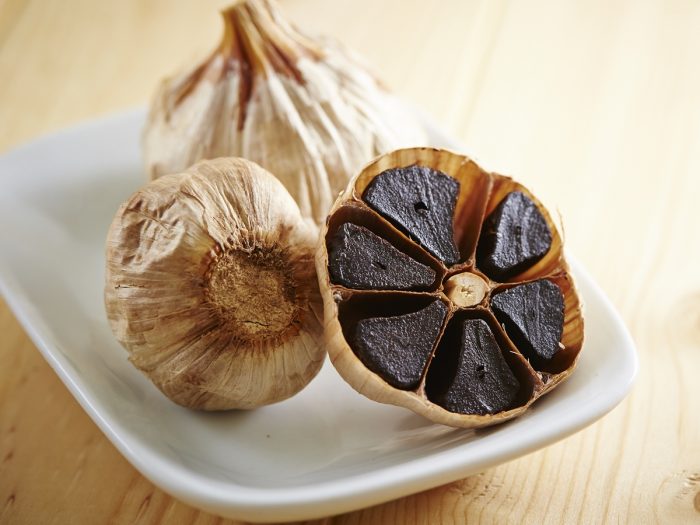 Whole and halved black garlic in a white dish on wood