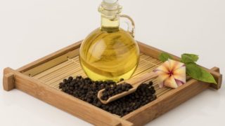 A jar of black pepper oil with a wooden of black peppercorns and flowers on a wooden tray