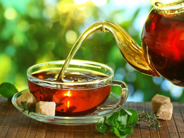 Black tea being poured out from the teapot with ice cubes and mint leaves on the table