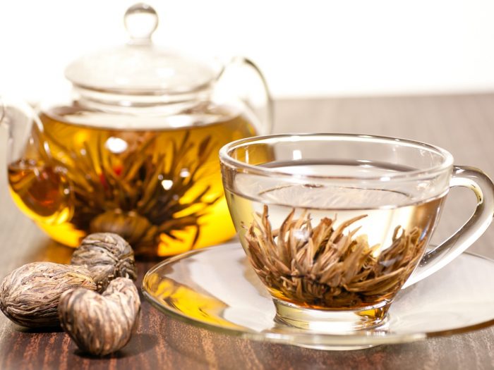 A cup of blooming tea kept beside a teapot containing blooming tea