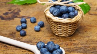 A small wooden basket and wooden spoon filled with blueberries on a wooden table