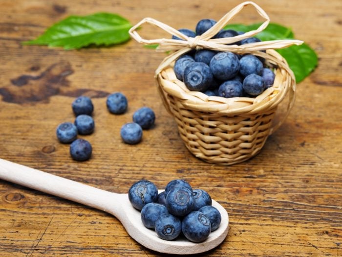 A small wooden basket and wooden spoon filled with blueberries on a wooden table