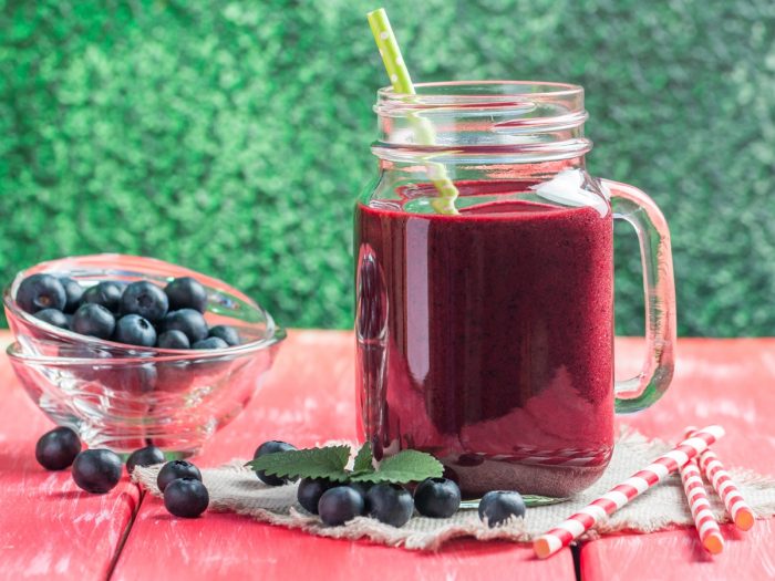 A mason jar filled with blueberry juice with few blueberries aside