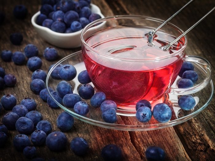 A cup of blueberry tea with strainer inside and blueberries around