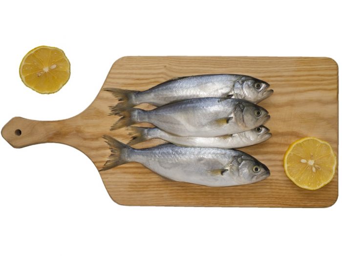 Bluefish stacked on a wooden board with lime slices