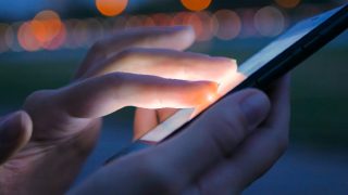Person using a phone emitting blue light at dusk