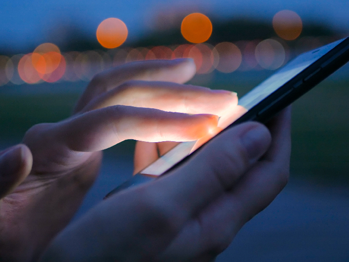 Person using a phone emitting blue light at dusk
