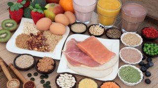 Fruits, vegetables, legumes, lentils, nuts, animal proteins, grains, and glasses of juices placed on a mat.