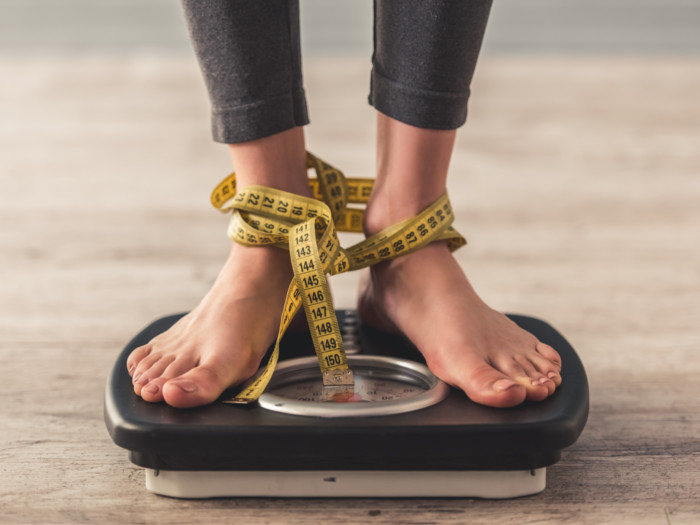 A woman on a weighing machine, her feet tied with a measuring tape