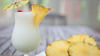 A glass of booch on the beach standing next to cut pineapples