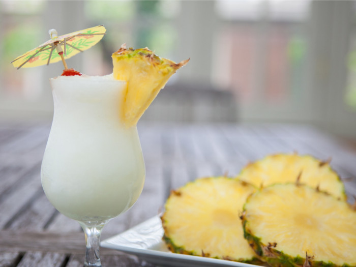 A glass of booch on the beach standing next to cut pineapples