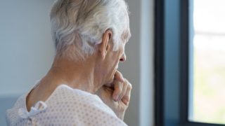 An older man sitting in a hospital robe looking out the window