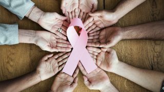 Group of hands holding a breast cancer awareness ribbon