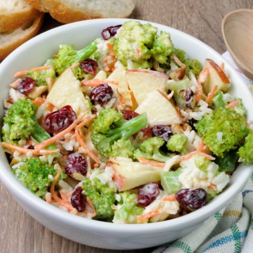 broccoli cranberry salad with sliced apples in a white bowl