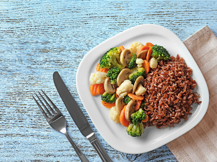Plate with tasty brown rice and vegetables on wooden table