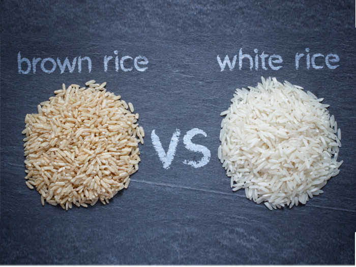 A flat lay close up shot of brown rice vs white rice against a dark background