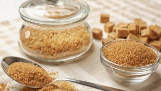 A jar of granulated brown sugar, a spoon and bowl of brown sugar powder, and brown sugar cubes on a cloth