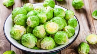 Fresh green Brussels sprouts in a ceramic bowl on a wooden table