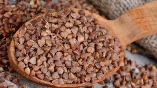 Close-up of a wooden spoon filled with buckwheat on a wooden table