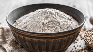 Buckwheat flour in a bowl with napkin at bottom with buckwheat in a spoon