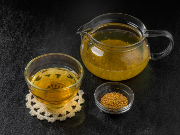 A close-up picture of a kettle, buckwheat seeds, and buckwheat tea kept in line next to each other