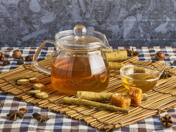 Small transparent kettle and tea cup filled with tea and surrounded by burdock root