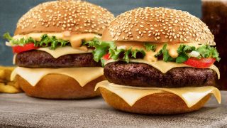 Side view of two cheeseburgers on a wood surface.