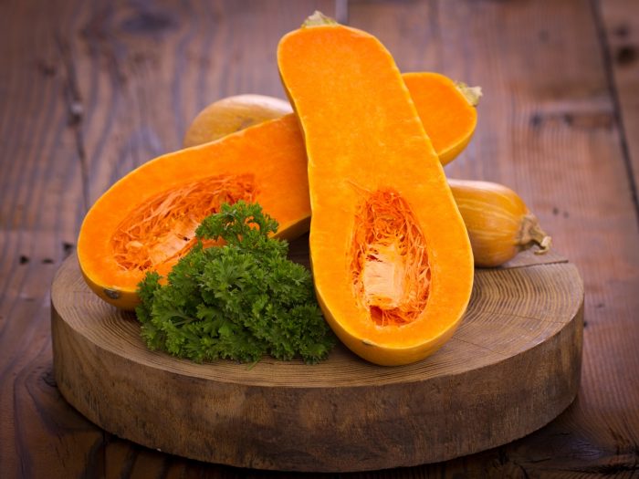 Half-cut butternut squash on a round wooden cutting board