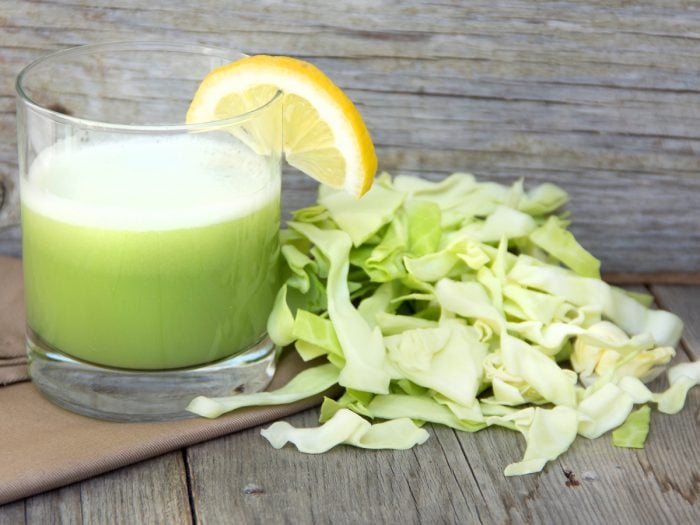 A glass of fresh cabbage juice with sliced cabbage on a wooden table