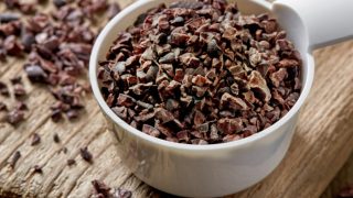 Cacao nibs in a white measuring cup on a wooden counter