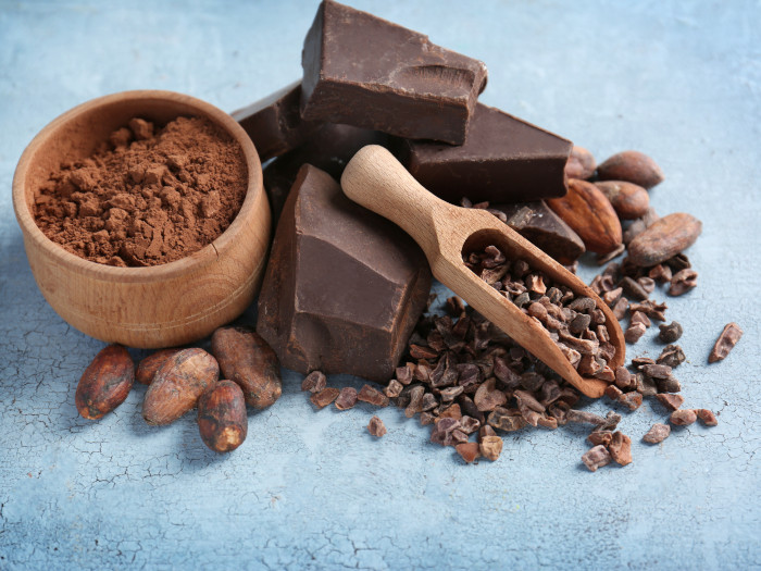 Loose cocoa beans, powder, and sliced chocolate bits on a blue surface
